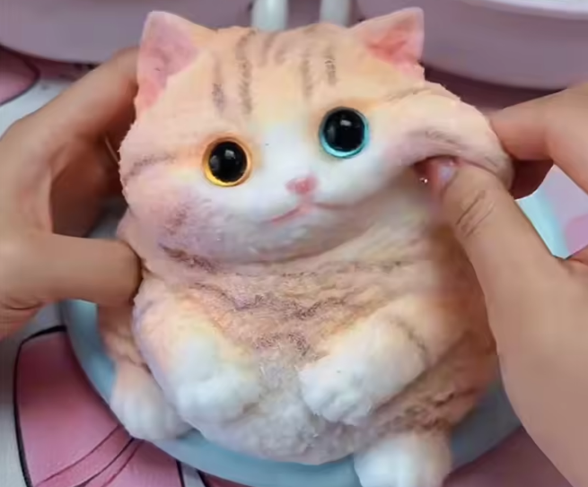 Toy cat being held by hands with a pink background
